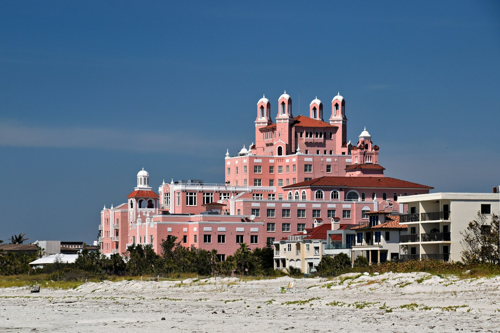 The pink Don CeSar hotel behind the white sand of St. Pete Beach under a blue sky
